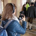 Lustwandler begeben sich vom Vestibül des Neuen Schlosses Schleißheim zum beeindruckenden Treppenaufgang. Sie sind mit Kameras und Smartphones bewaffnet.